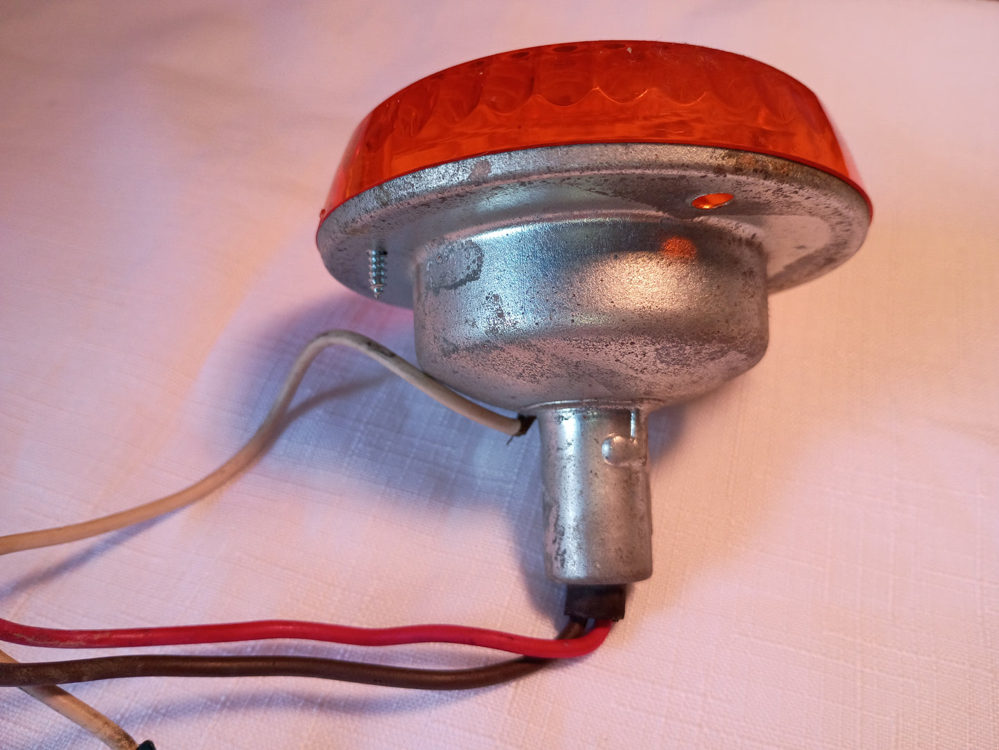 A vintage-style amber warning reflector light with a silver metal base and attached wires, photographed on a light fabric surface.