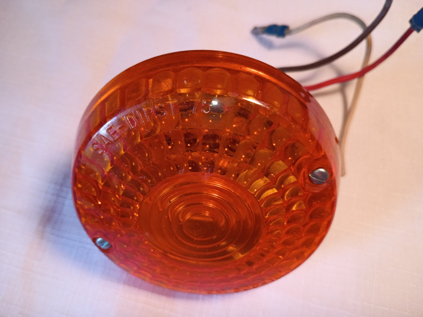 An orange circular plastic marker light with a textured lens and attached red, black, and white wires, photographed on a light-colored surface.