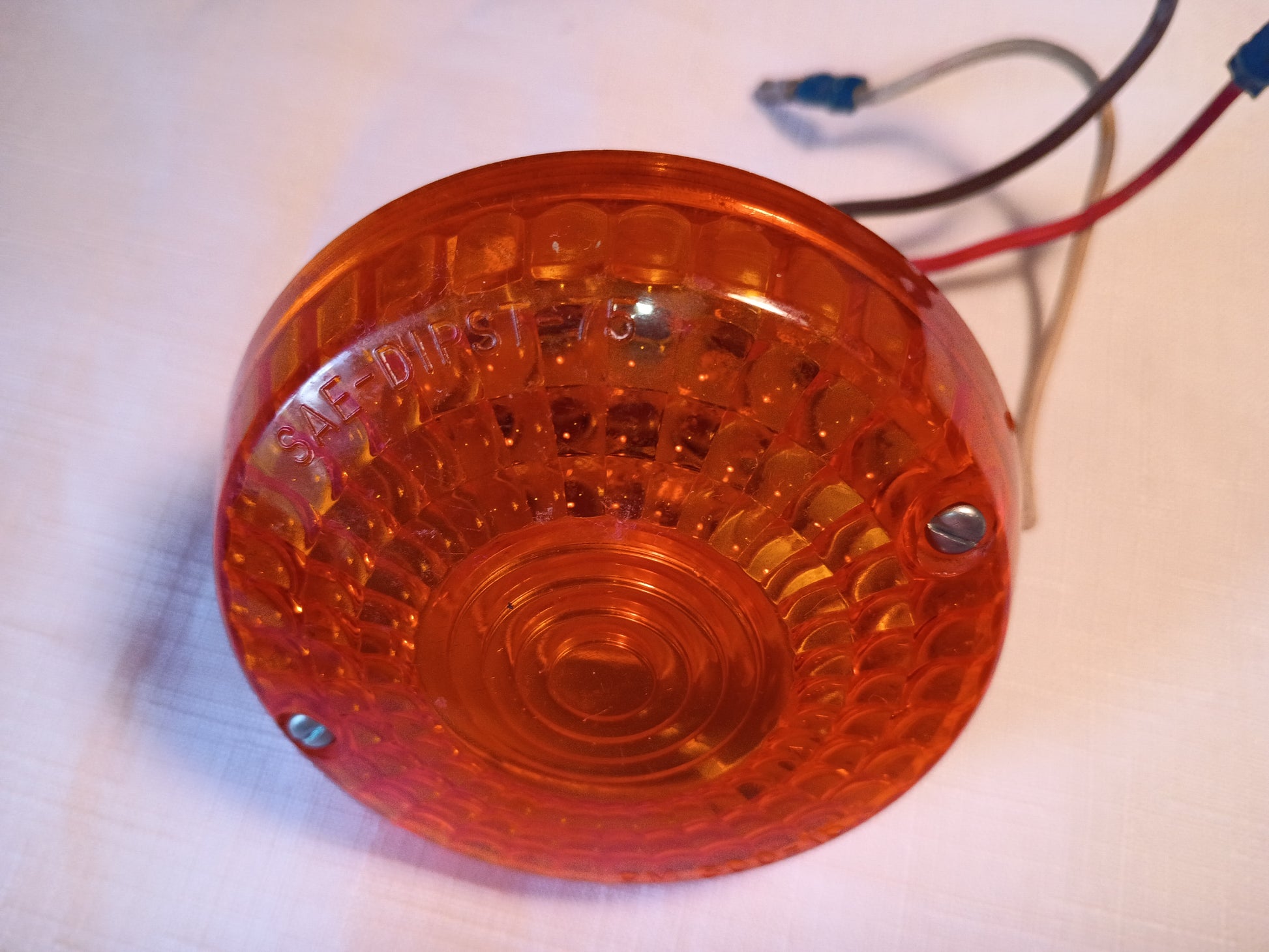 An orange circular plastic marker light with a textured lens and attached red, black, and white wires, photographed on a light-colored surface.