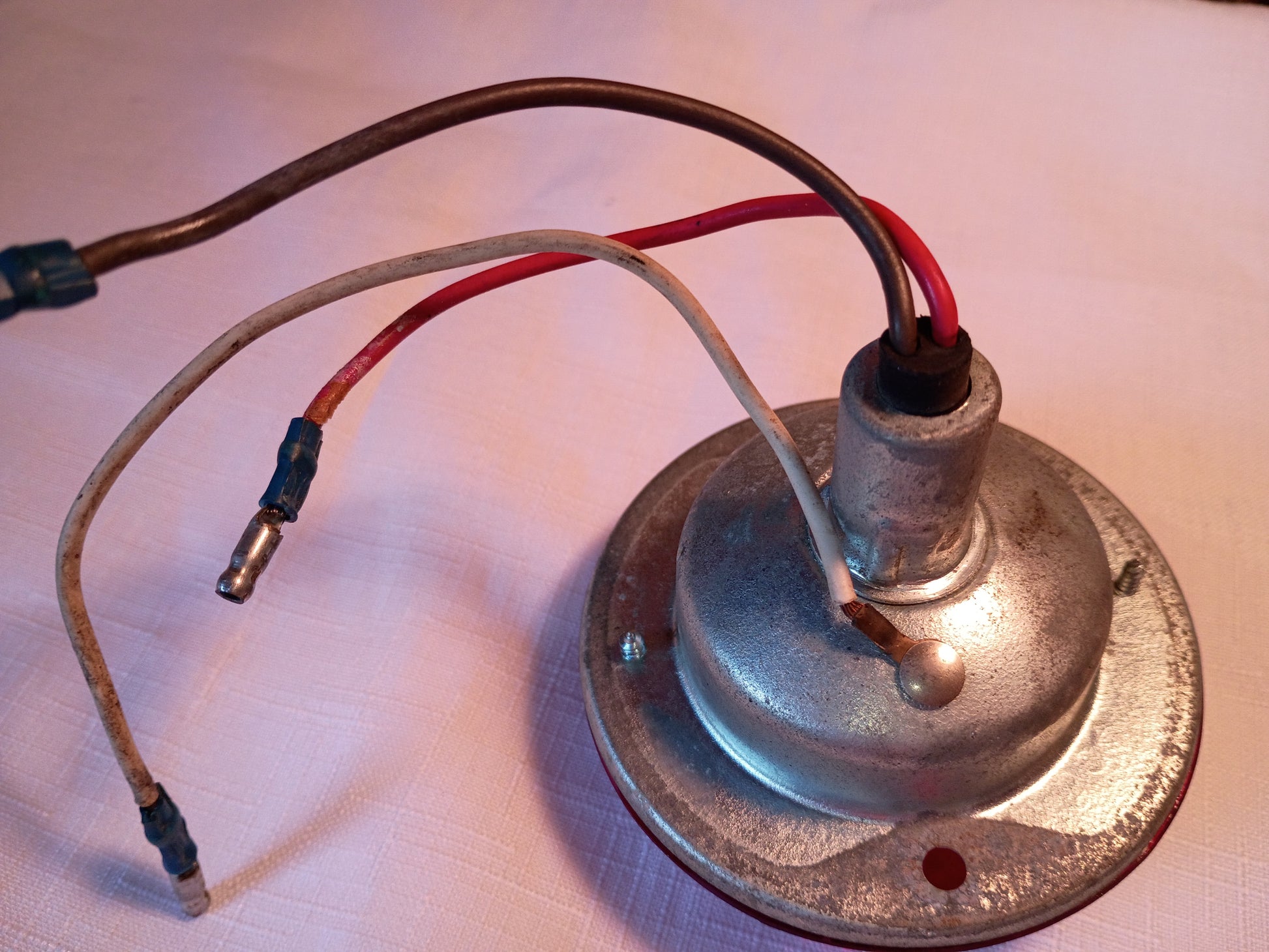 A vintage metal lamp socket or light fixture base with attached wires, photographed on a light-colored fabric surface.